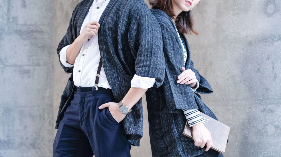 A man and a woman modeling textured charcoal grey hand-cranked kimono jackets in a close-up pose against a concrete wall at Grandmama Store in Hong Kong.