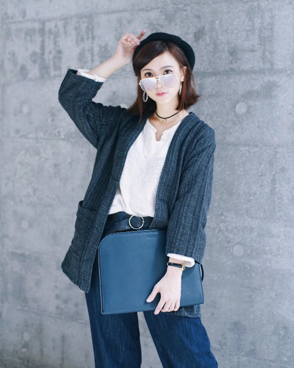 A woman poses for a street style photo, wearing a dark blue hand-cranked woven kimono jacket in the 'Miho Matsubara' color, paired with a white top, denim jeans, a black beret, sunglasses, and holding a blue laptop case at Grandmama Store in Hong Kong.