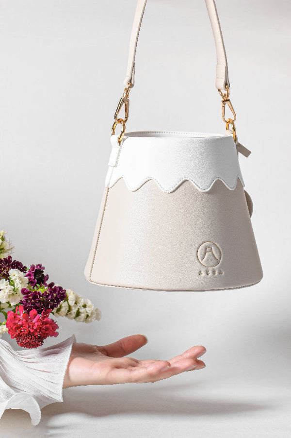 Beige leather Mt. Fuji Goen Bag in Tea colourway floating above a hand with flowers at Grandmama Store in Hong Kong.